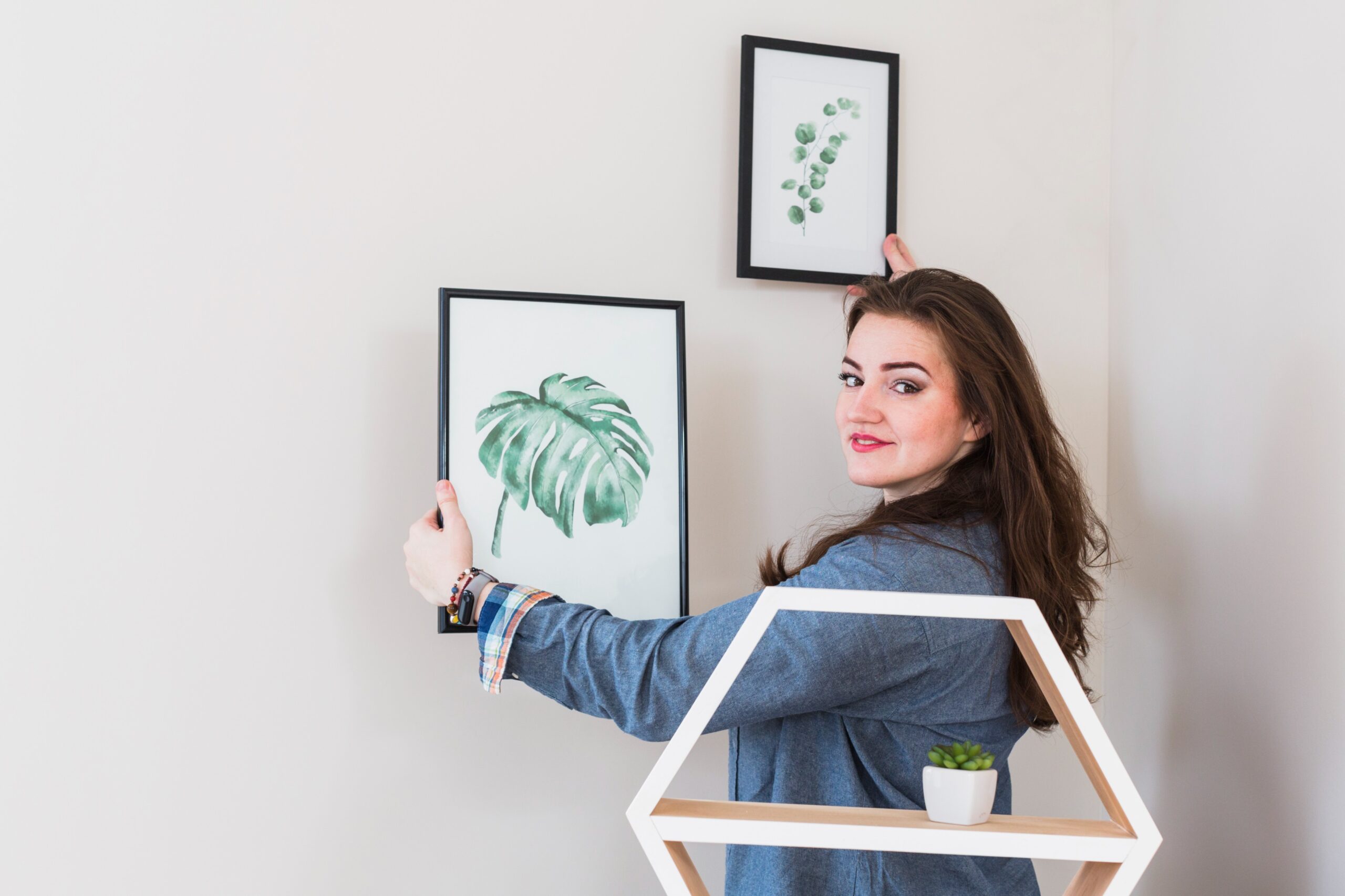 portrait-young-woman-fixing-picture-frame-wall-looking-camera (1)
